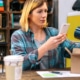 Banner of young female entrepreneur taking photo with cell of a mug for client of her online store