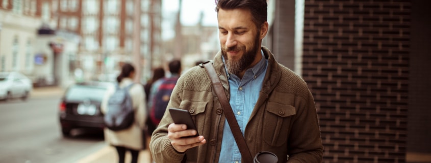 Man walking with coffee and using smartphone in city street