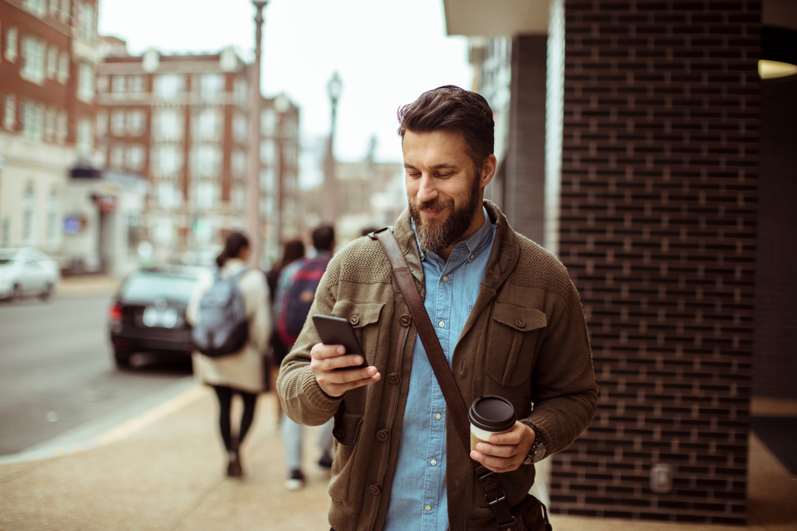 Man walking with coffee and using smartphone in city street