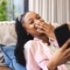 Young African American woman laughs while looking at her phone, reclining on a couch